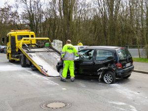 ein Mann lädt dort ein kaputtes Auto auf einen Transporter