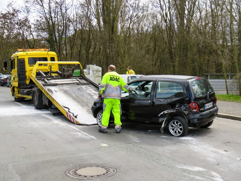 ein Mann lädt dort ein kaputtes Auto auf einen Transporter