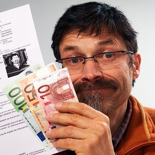 Ein Mann mit Brillen hält einen Bußgeldschein und 160 EUR in Bargeld