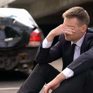 Verzweifelter Mann sitzt Asphalt nach einem Autounfall auf dem Hintergrund