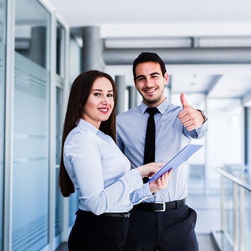 Ein Mann und eine Frau Serviceberater stehen lächelnd in einem Büro, in dem die Frau einige Seiten zeigt und der Mann einen Daumen hoch gibt