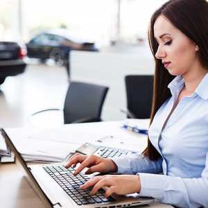 Eine Serviceberaterin im blauen Hemd sitzt vor einem Computer im Autohaus und schreibt