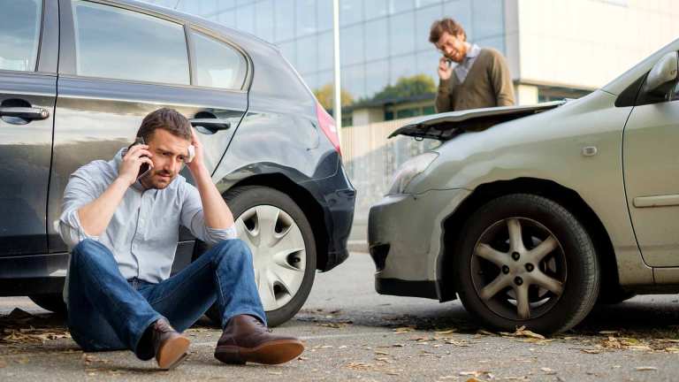 Nach einem Auffahrunfall telefonieren zwei Männer neben ihren Fahrzeugen.