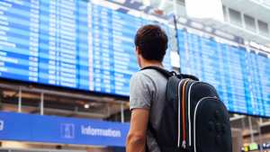 Ein Passagier mit Rucksack schaut auf eine Informationstafel im Flughafengebäude.