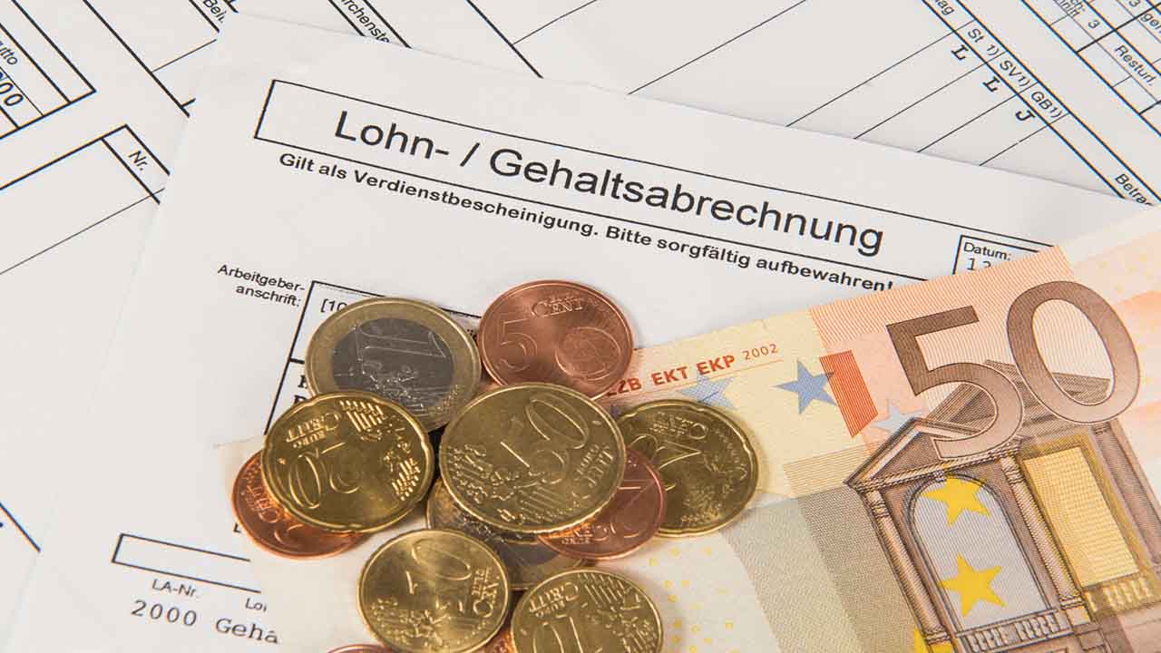 Ein 50 Euro Schein und mehrere Münzen liegen auf einem Formular mit der Aufschrift Lohn- / Gehaltsabrechnung.