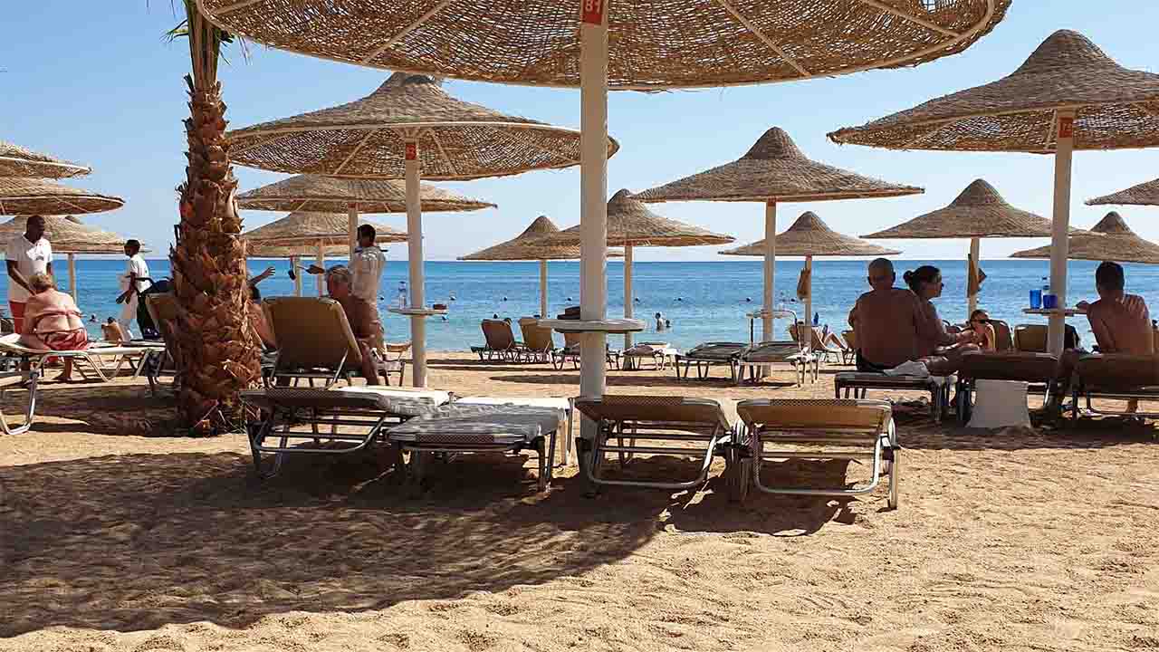 Strand mit Sonnenschirmen aus geflochtenem Bast und einige Badegäste.